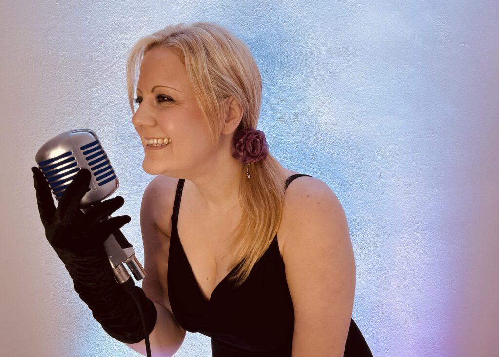Tracy is looking to the side whilst holding a vintage microphone and singing as a wedding singer suffolk.
