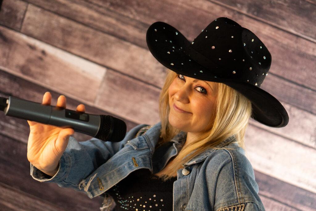 Tracy is wearing a cowboy hat and holding a mic ready to sing as a country tribute act essex.